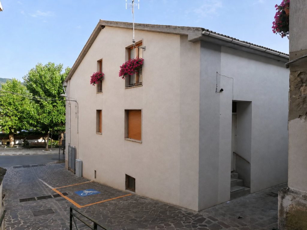 L'edificio della dimora restaurato, visto dallo slargo, con le fioriere alle finestre e l'ingresso laterale.